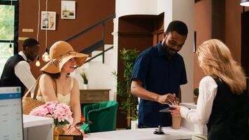 hotel invitados comprobación en a recepción, firma electrónico documentos en tableta. viajeros a frente escritorio relleno en registro documentos para habitación reserva en verano playa día festivo. Mano disparo. foto