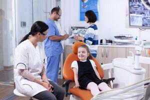 Shy little girl looking up at dentist doctor waiting teeth cavity treatment. Child with her mother during teeth check up with stomatolog sitting on chair. photo