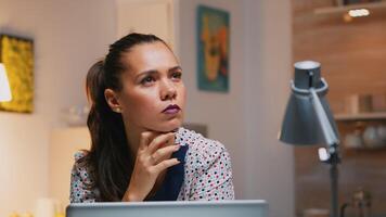 Portrait of businesswoman thinking of email answer working at home sitting on kitchen desk. Close up of busy employee using modern technology network wireless doing overtime reading writing, searching photo