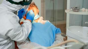 dentista técnico en bata Encendiendo el lámpara para examinando mayor paciente durante global covid-19 pandemia. asistente y ortodoncia médico vistiendo proteccion traje, cara proteger, máscara y guantes foto