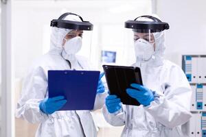 Doctors taking notes wearing ppe suit and face mask in hospital Medical colleagues wearing professional gear against infection with coronavirus as safety precauition. photo