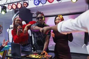 Musicians performing on stage, interacting with crowd and bumping fists. Electronic music band using dj station for mixing tracks live and engaging audience at nightclub party photo