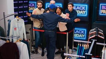 Anxious clients push guard at store to enter mall for black friday discounts and deals, standing behind red tape at entrance. Diverse crazy people being aggressive to open shopping center. photo