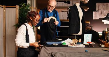 Student and tailor cutting fabric, learning to design handmade clothes in atelier. Tailoring apprentice using scissors and preparing material to manufacture items with old couturier. photo