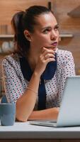 Thinking at next project while working remotly from home, reading the tasks using laptop sitting in the kitchen. Busy focused employee using modern technology network wireless doing overtime for job typing writing, searching photo