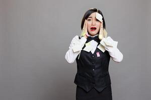 Exhausted busy restaurant manager in uniform overloaded with tasks panicking and looking at camera. Catering service stressed asian waitress with sticky notes on face portrait photo