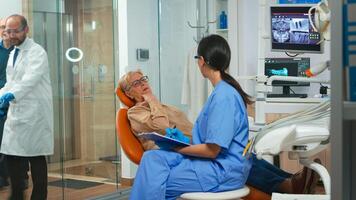Patient with tooth pain explaining dental problem to nurse and indicating at toothache. Assistant taking notes on clipboard and preparing for stomatologic examination. Orthodontic office in modern clinic photo