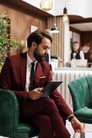 White collar worker checking files on tablet, working while he waits to do check in process at hotel. Businessman review notes before attending important meeting, business trip. photo