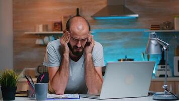 Freelancer suffering from headache touching temple after hours of work on laptop at home in modern kitchen. Busy focused employee using modern technology network wireless doing overtime working photo