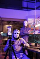 Anonymous criminals streaming web threat on smartphone, doing cyberattack. Hackers committing internet crime while recording fraud video on mobile phone and asking victim for payment photo