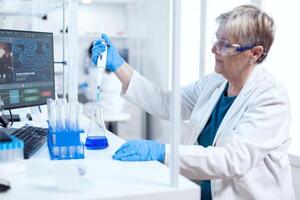 Senior chemist woman using molecular dropper during healthcare experiment. People in innovative pharmaceutical laboratory with modern medical equipment for genetics research. photo