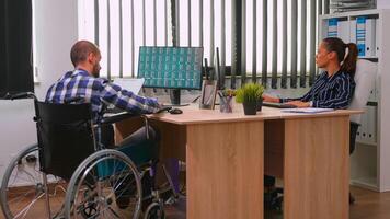 Paralysed financial expert sitting in wheelchair analysing economy statistics of company in business office discussing with woman manager. Handicapped, immobilized businessman using modern technology. photo