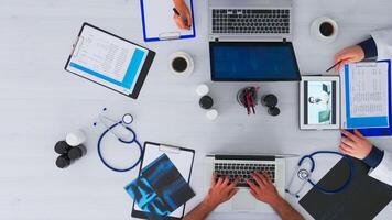 Top view of resident physicians advising with doctor using videocall sitting on desk in clinic with medical equipment. Talking with specialist on videomeeting online conference on copy space, flat lay photo