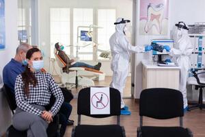 Stomatology dentist dressed in ppe suit taking patient x-ray from receptionist in clinic hallway, keeping social distancing during global pandemic with coronavirus. photo