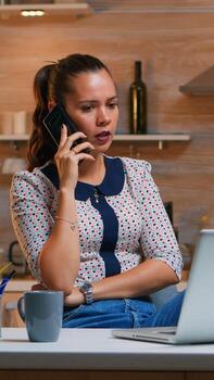 Remote employee speaking at phone while working at laptop late at night. Busy focused freelancer using modern technology network wireless doing overtime for job reading writing, searching taking break photo