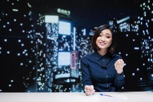 Night show host on live broadcast addressing global news topics from newsroom, discussing about daily events. Asian presenter reporting media information to provide latest tv content. photo