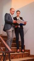 Office executive holding clipboard discussing with company manager on staircase of business building analysing reports. Group of professional businesspeople working in modern financial workplace. photo