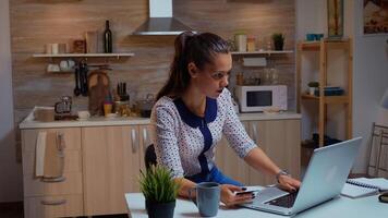 Hispano mujer utilizando crédito tarjeta en hogar cocina a hacer en línea pago. empleado haciendo pago transacción desde hogar en digital cuaderno conectado a Internet trabajando tiempo extraordinario para trabajo foto