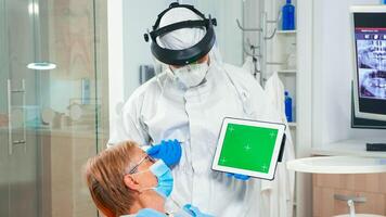 Dentist in coverall pointing at green screen display during coronavirus epidemic. Explaining using monitor with chroma key izolated chroma pc key mockup greenscreen display mock-up touchscreen photo