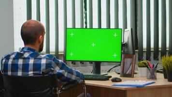 Immobilized businessman in wheelchair using computer with chroma key for videomeeting. Handicapped disabled freelancer looking at pc with green screen, mockup, key talking with remotely colleagues photo