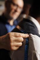 Expert precise craftsman taking fit measurements on sartorial piece using tape. Precise experienced tailor helping customer with custom made stylish formal suit, close up photo