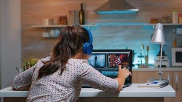 Video editor wearing headset and working from home at digital project sitting in the kitchen. Videographer editing audio film montage on professional laptop sitting on desk in midnight photo