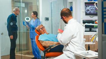 Stomatologist holding plaster model of the mandible speaking with elderly patient. Dentist showing the correct dental hygiene using mock-up of skeleton of teeth, sample of human jaw with toothbrush photo