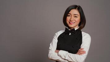 Restaurant hostess posing with confidence in studio, standing with arms crossed over grey background. Asian waitress barista with gourmet serving expertise smiling on camera. Camera B. photo