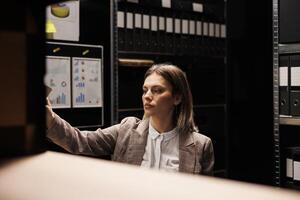 Manager working with bureaucracy files, analyzing bookkeeping record searching for management report. Bookepper standing overhours in arhive room, organizing depository documents photo