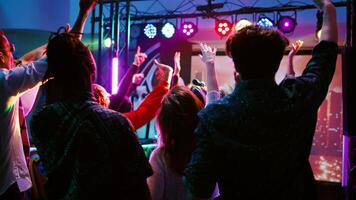 alegre adultos teniendo divertido con DJ música en panel estación, bailando debajo disco luces en danza piso. joven multitud de amigos ir de fiesta y clubbing con moderno miedoso latidos Mano disparo. foto