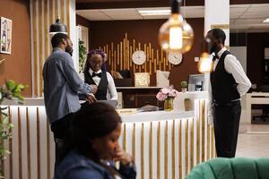 Friendly welcoming female receptionist helping tourist with check-in procedure at front desk. African American hotel staff assisting guest at reception, customer service in hospitality industry photo