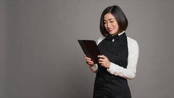 Asian restaurant server checking all table reservations on tablet, browsing through clients information on website. Waitress looking at online webpages to see availability. Camera A. photo