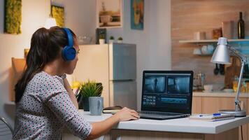 Freelancer content creator working overtime from home to respect deadline. Woman videographer editing audio film montage on professional laptop sitting on desk in modern kitchen in midnight photo