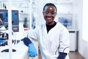 Portrait of professional african scientist smiling at camera in sterile laboratory. Multiethnic team of researchers working in microbiology lab testing solution for medical purpose. photo