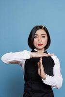 Serious asian waitress in uniform showing timeout sign with hands, asking to take break portrait. Young woman receptionist making interruption and pause gesture while looking at camera photo