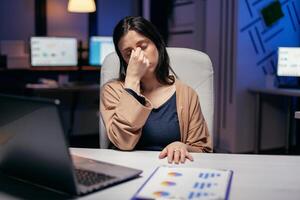 Businesswoman having a migraine in the course of overtime hours for job to work in deadline. Employee falling asleep while working late at night alone in the office for important company project. photo