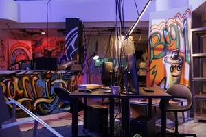 Internet criminals abandoned warehouse with graffiti at night time. Computers on desks and equipment for hacking and malware coding in hackers dark hideout room with neon light photo