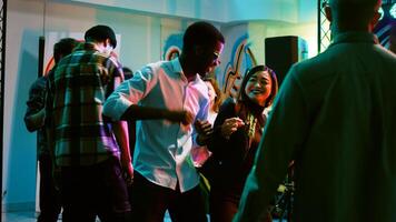 Happy men and women dancing at club, having fun jumping on electronic music. Group of people doing dance moves at discotheque and attending disco party with friends. Handheld shot. photo