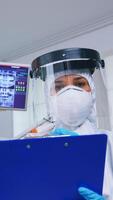 Pov of patient getting dental treatment in dentist office with new normal, doctor taking notes on clipboard before examining. Stomatolog wearing safety gear against coronavirus during heatlhcare check photo