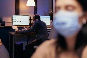 Entrepreneur working in the course of covid19 outbreak wearing face mask. Woman following social distancing rules due to coroanvirus pandemic while working late hours at the office. photo