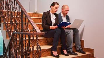 Overworked exhausted business people using laptop working on difficult deadline sitting on stairs in office building. Group of professional successful businesspeople walking in financial workplace. photo