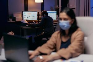 Office colleagues talking on the phone with client to finish a deadline in the course of global pandemic. Woman following social distancing rules due to coroanvirus pandemic while working late hours at the office. photo