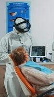 Dentist wearing protection equipmentin dental office examining x-ray image on tablet during global pandemic. Medical team with face shield, coverall, mask reviewing radiography using digital device photo