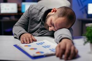 Overworked hardworking businessman resting head on the tablet. Workaholic employee falling asleep because of while working late at night alone in the office for important company project. photo