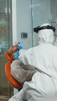 Nusre with face shield measuring old woman temperature before dental examination during global pandemic. Concept of new normal dentist visit in coronavirus outbreak wearing protective suit and face shield photo