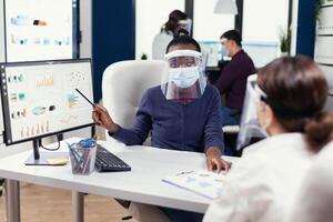Business people discussing the charts and graphs showing their success. Multiethnic team working in company with new normal respecting social distance because of global pandemic with coronavirus. photo