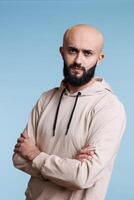 Serious arab man frowning eyebrows while posing with crossed arms studio portrait. Confused person with tensed facial expression standing with folded hands and looking at camera photo