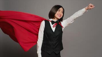 Front desk operator feeling strong with a superhero cape on camera, posing with confidence and showing power in studio. Hotel concierge wearing a red hero cloak, hospitality industry. Camera A. photo