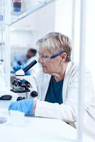 Concentrated senior scientist conducting genetic experiment using microscope. Elderly researcher carrying out scientific research in a sterile lab using a modern technology. photo