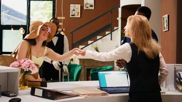 Hotel guests taking key card from front desk staff, finishing with check in registration procedure. Receptionist and bellboy providing luxury service for travellers. Handheld shot. photo